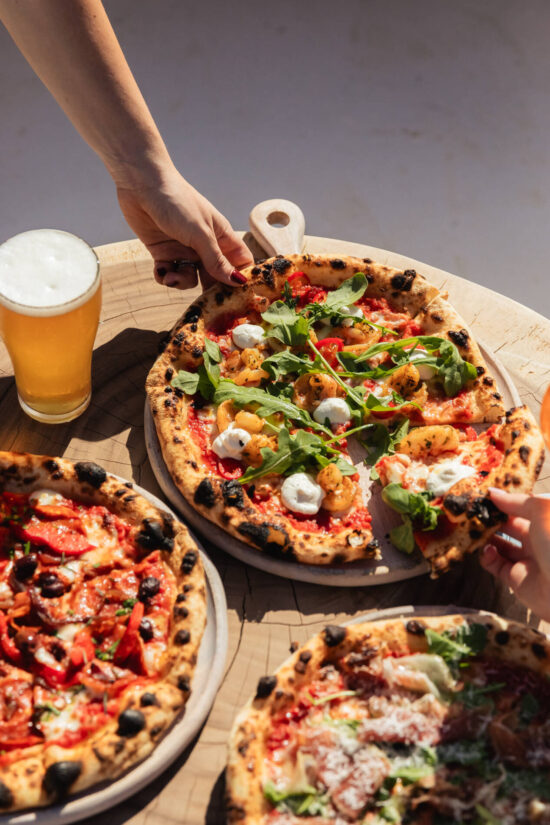 Wood-fired pizza at Aanuka Beach House with a beach view in the background, showcasing fresh ingredients and a coastal dining experience.